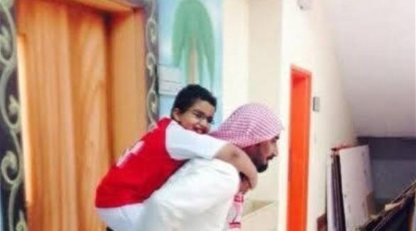 معلم سعودي يحمل طفلا من ذوي